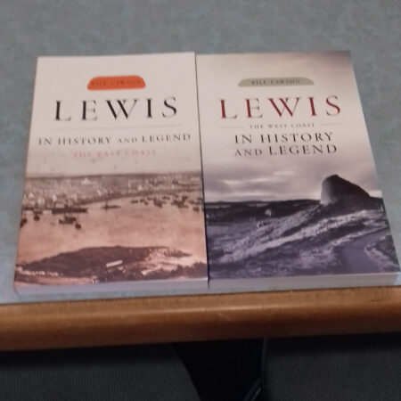 Two books titled *Lewis in History and Legend* are displayed side by side on a table. The book on the left has a sepia-toned landscape on its cover. The book on the right features an image of a coastline. Both books are authored by Bill Lawson.