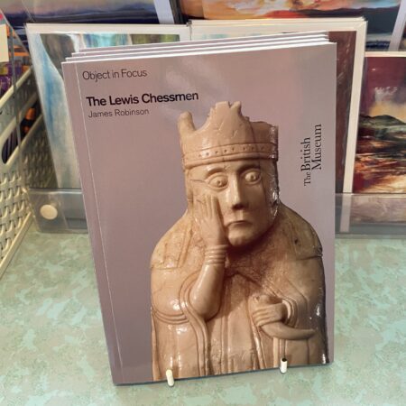 *The Lewis Chessmen* by James Robinson is a book published by the British Museum. The cover depicts one of the famous medieval chess pieces from the Lewis hoard, specifically a crowned figure with its head supported by its hand. The book provides historical and archaeological information about the Lewis Chessmen, which are 12th-century walrus ivory and whale tooth chess pieces discovered on the Isle of Lewis in Scotland. The British Museums logo appears along one side of the front cover.