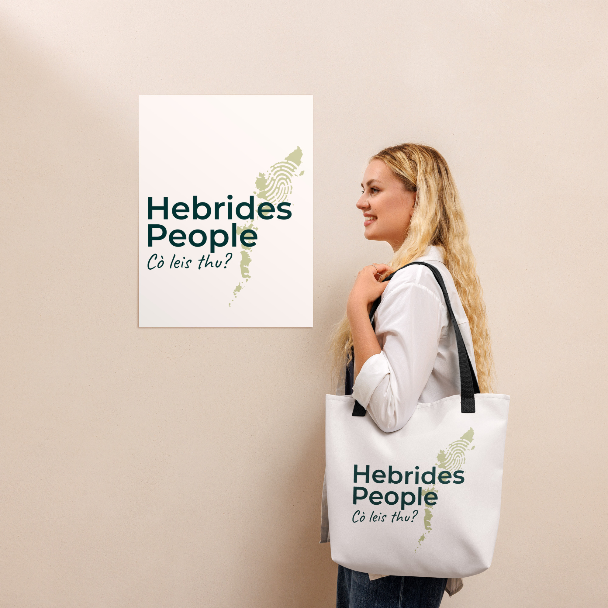 A woman with long blonde hair is holding a Tote bag labeled MacSween and printed with the words Hebrides People in green. She is standing beside a matching poster displayed on a beige wall. Both the tote bag and the poster feature an outline map of the Hebrides.