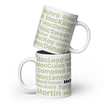 A white mug displays the Scottish surname MacInnes in light green and black text. Two mugs are shown, with one placed at an angle on top of the other. Product name: Mug - MacInnes.