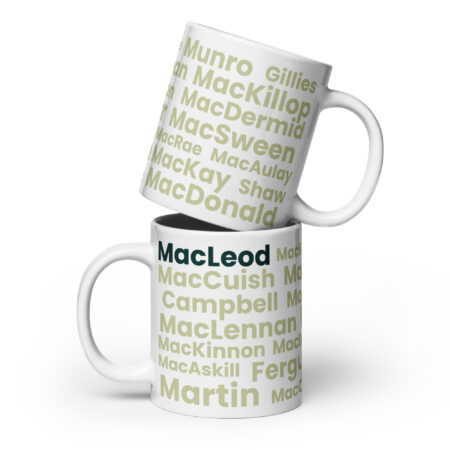 Two white mugs labeled MacLeod are stacked together. The bottom mug is upright, while the top mug rests at an angle with its rim on the lower mug. Each mug displays a series of Scottish surnames, with MacLeod prominently highlighted in bold dark green lettering.