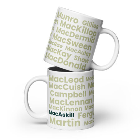 Understood. Here is a revised, factual description: Two white “Mug - MacAskill” mugs feature Scottish surnames such as MacDonald, MacLeod, and MacAskill printed in green and gray text. When stacked together, the design with the different surnames is clearly visible.