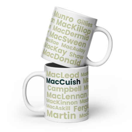 The image shows two white ceramic mugs stacked one on top of the other. Each mug is labeled with bold green and black text displaying Scottish surnames, including MacCuish, MacLeod, and MacDonald. The mugs have a standard cylindrical shape with a handle, and they are positioned against a plain white background. No additional objects or decorations are present in the scene.