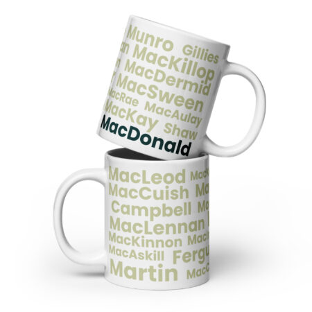 Two white ceramic mugs, labeled Mug - MacDonald, are shown. Each mug displays the Scottish surname MacDonald in bold green text. The top mug is positioned at an angle, resting on the lower mug. The display emphasizes the surname in a prominent and legible font.