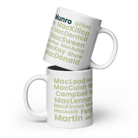 Certainly. Here is a factual description: Two white Mug - Munro mugs are stacked. Each mug features a list of surnames, including Munro, MacLeod, and Martin. The surnames are printed in green and tan text on a white background.