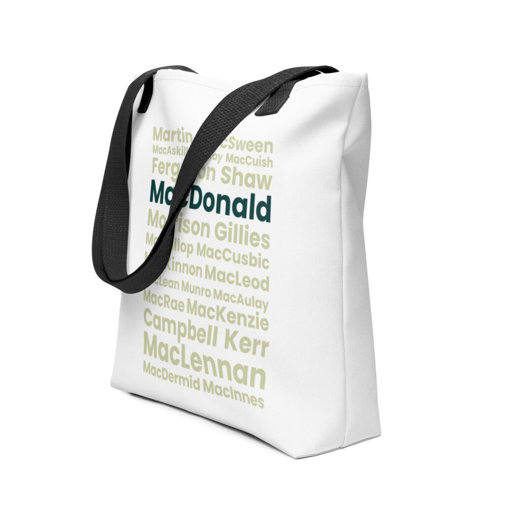 The Tote bag - MacDonald is a white bag with black straps. The bag features Scottish surnames, including MacDonald, Campbell, and MacLennan. These names are printed in assorted shades of green, using various text styles and font sizes.