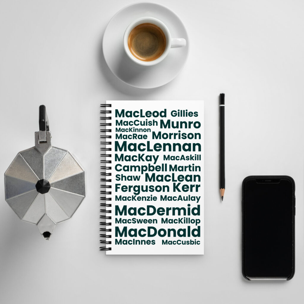 Understood. Here is a factual description: The Notebook - Common Harris Surnames is positioned on a white desk. Next to it are a cup of coffee, a moka pot, and a smartphone.