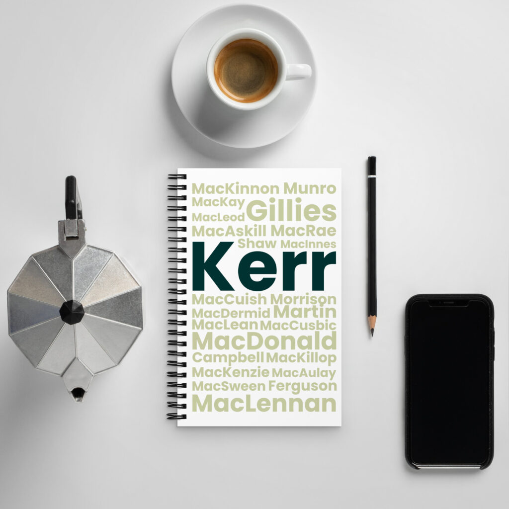 A flat lay photo displays a coffee cup, a moka pot, a smartphone, and the Notebook - Kerr, which features various Scottish surnames in different font sizes. The surname Kerr is prominently highlighted in bold blue on the notebook cover.