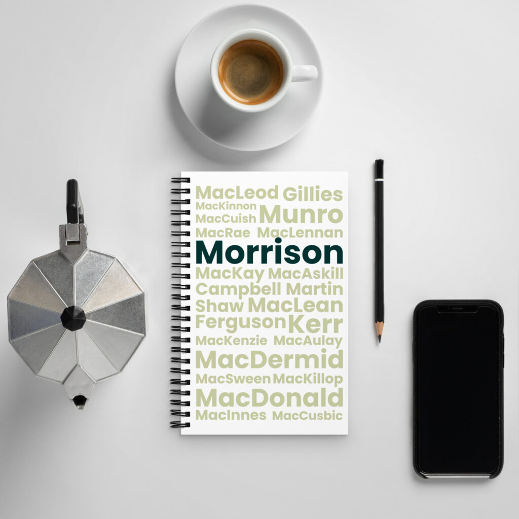 Here is a factual description of the scene: The Notepad—labeled Morrison—is positioned on a white table alongside several items. Resting near the notepad are a pen, a coffee cup, and a moka pot. Also arranged close by is a smartphone. All items appear neatly organized on the tabletop.