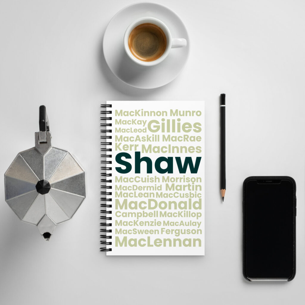 The Notebook - Shaw, with the surname Shaw rendered in bold, is situated on a white table. The surrounding items include a coffee cup, a stovetop espresso maker, a black pencil, and a smartphone.
