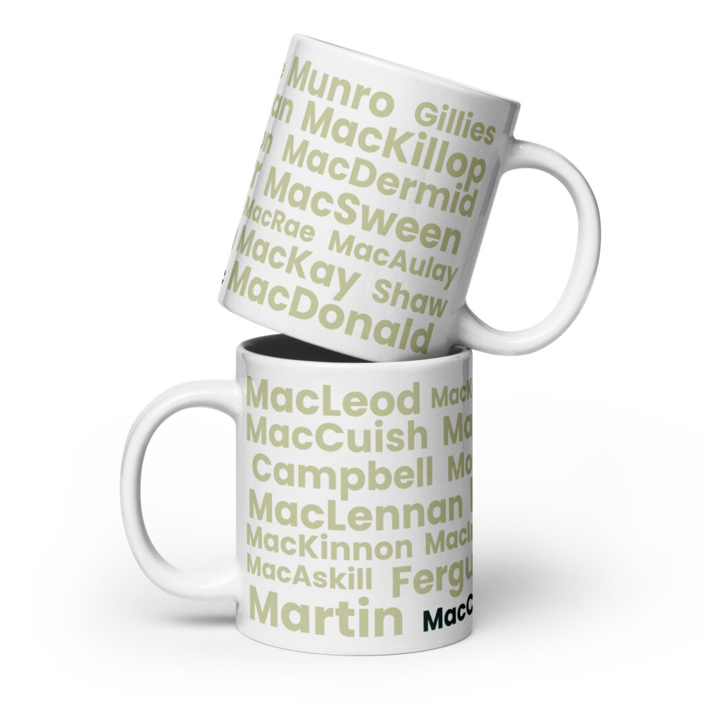 Two white Mug - MacCusbic mugs are stacked. Each mug features bold green and gray Scottish surnames—MacLeod, MacDonald, Munro, and MacCusbic—set against a clean white background.