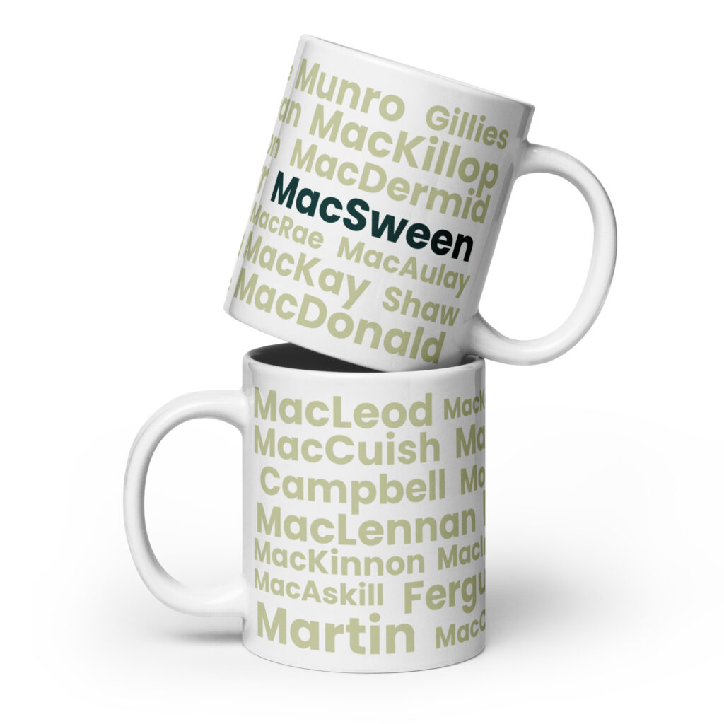 Understood. Here is a factual description: Two white Mug - MacSween mugs are stacked together against a white background. Each mug features the word MacSween printed in bold black text. The design and color of both mugs are identical, with no additional decorations or patterns visible.