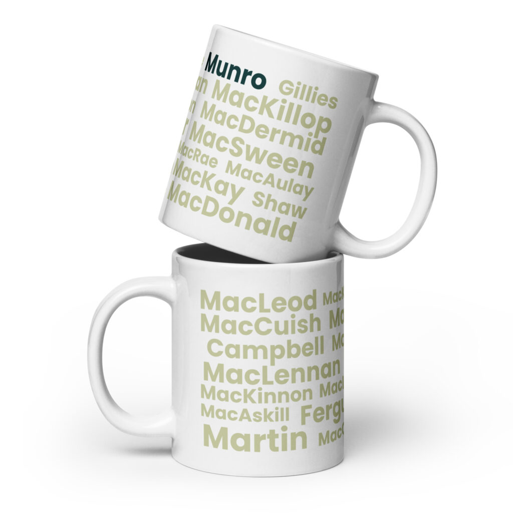 Certainly. Here is a factual description: Two white Mug - Munro mugs are stacked. Each mug features a list of surnames, including Munro, MacLeod, and Martin. The surnames are printed in green and tan text on a white background.