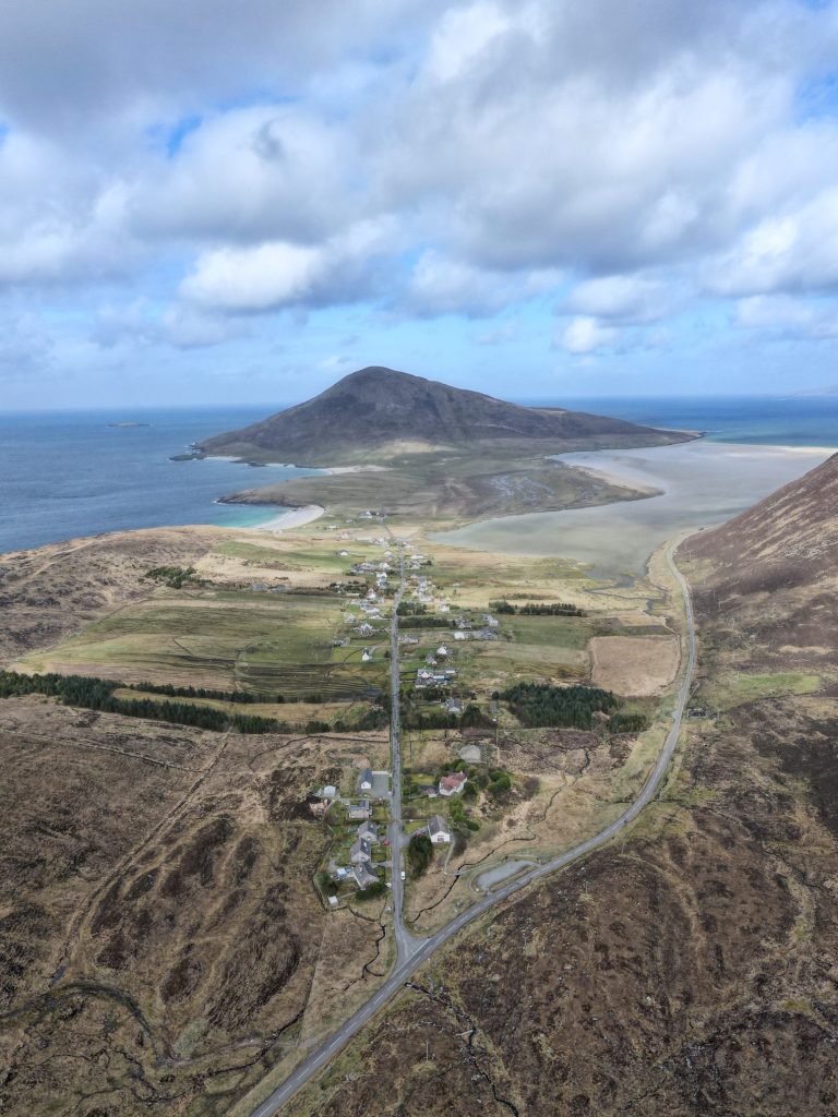 Aerial view Northton village on a narrow strip of land with surrounding fields, winding roads, coastal waters, and distant mountain.